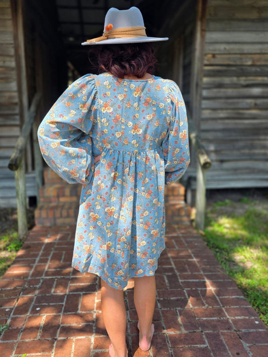 Front and back view of a washed floral denim dress featuring long puff sleeves, tie-front neckline, and a relaxed above-the-knee silhouette.