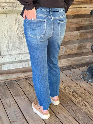 Person wearing blue jeans standing on a wooden deck.