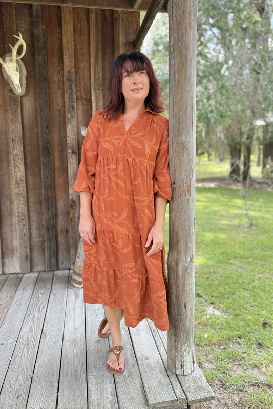 Woman in a rust-colored dress standing on a wooden deck with a natural background