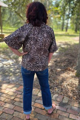 Person wearing a leopard print top and blue jeans standing outdoors on a brick path.