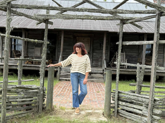 Woman wearing a beige and cream striped short-sleeve V-neck knit top with relaxed fit, paired with blue jeans outdoors.