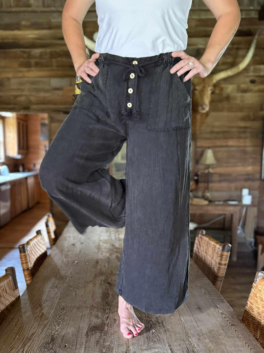 Woman wearing washed black wide-leg pants with rope drawstring tie, button-front detail, and relaxed fit.