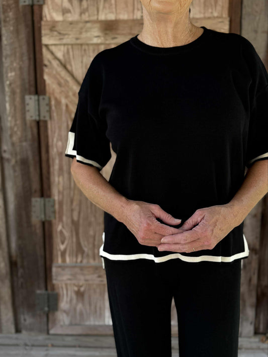 Woman wearing a black two-piece knit lounge set with wide-leg pants and short-sleeve top trimmed in ivory.