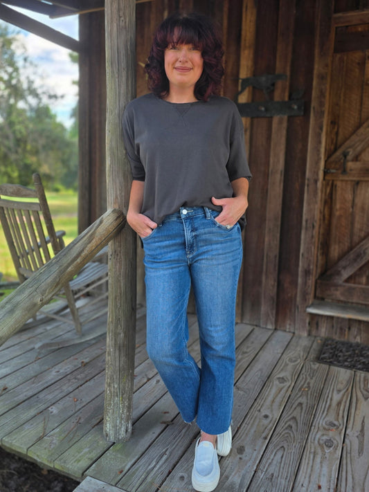Woman wearing a gray terry crew neck shirt with half sleeves, styled casually with blue jeans and white slip-on sneakers.