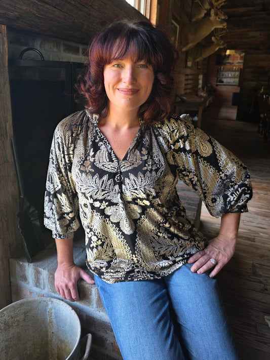 Woman standing in a rustic interior setting with wooden walls and a window.
