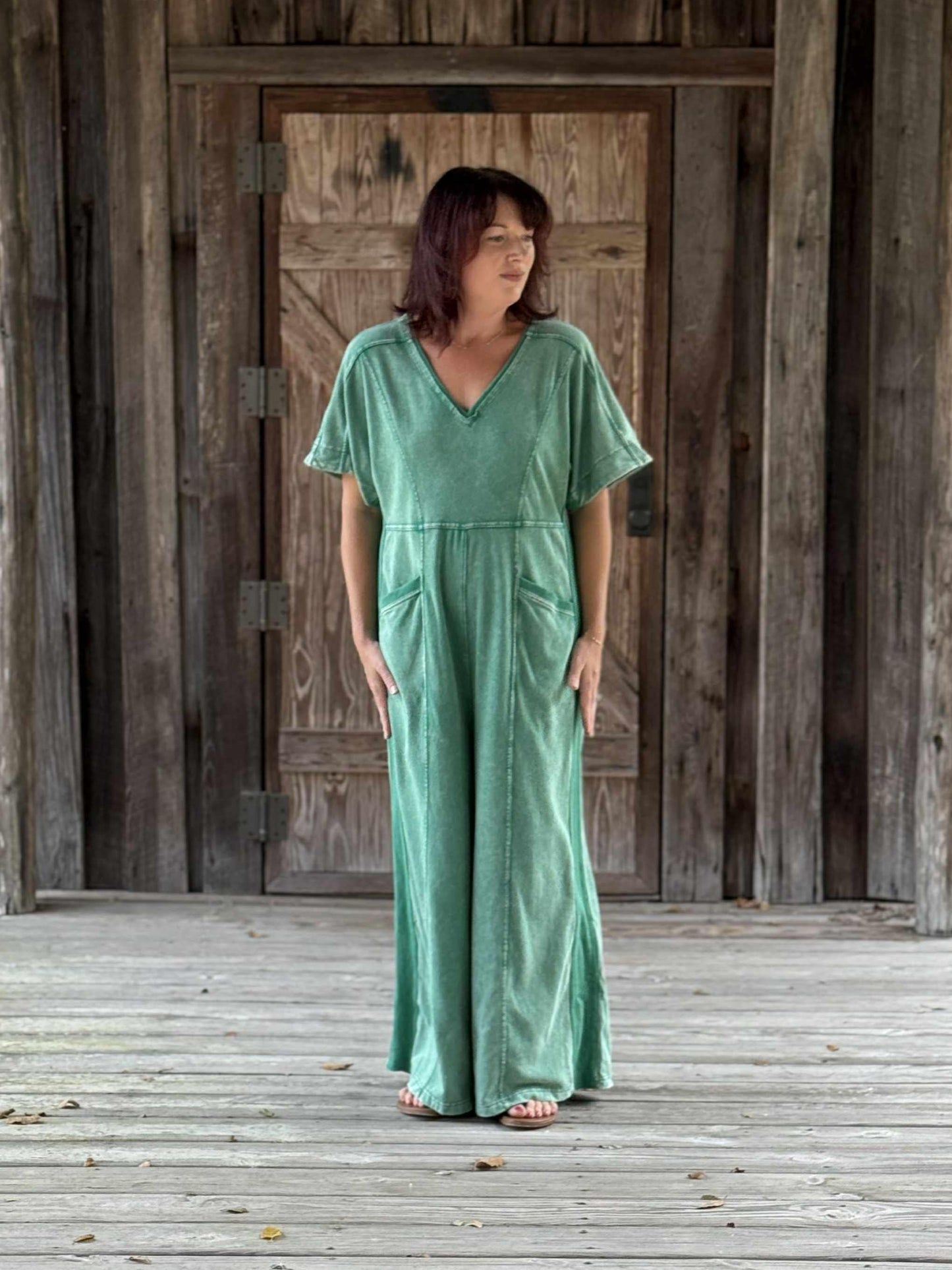 Woman wearing a green V-neck wash jumpsuit with wide legs, French terry fabric, rib contrast, and keyhole back detail.