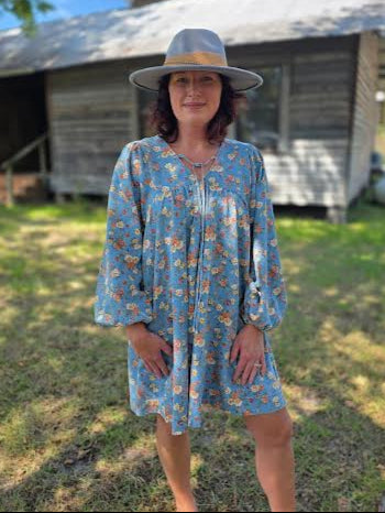 Front and back view of a washed floral denim dress featuring long puff sleeves, tie-front neckline, and a relaxed above-the-knee silhouette.