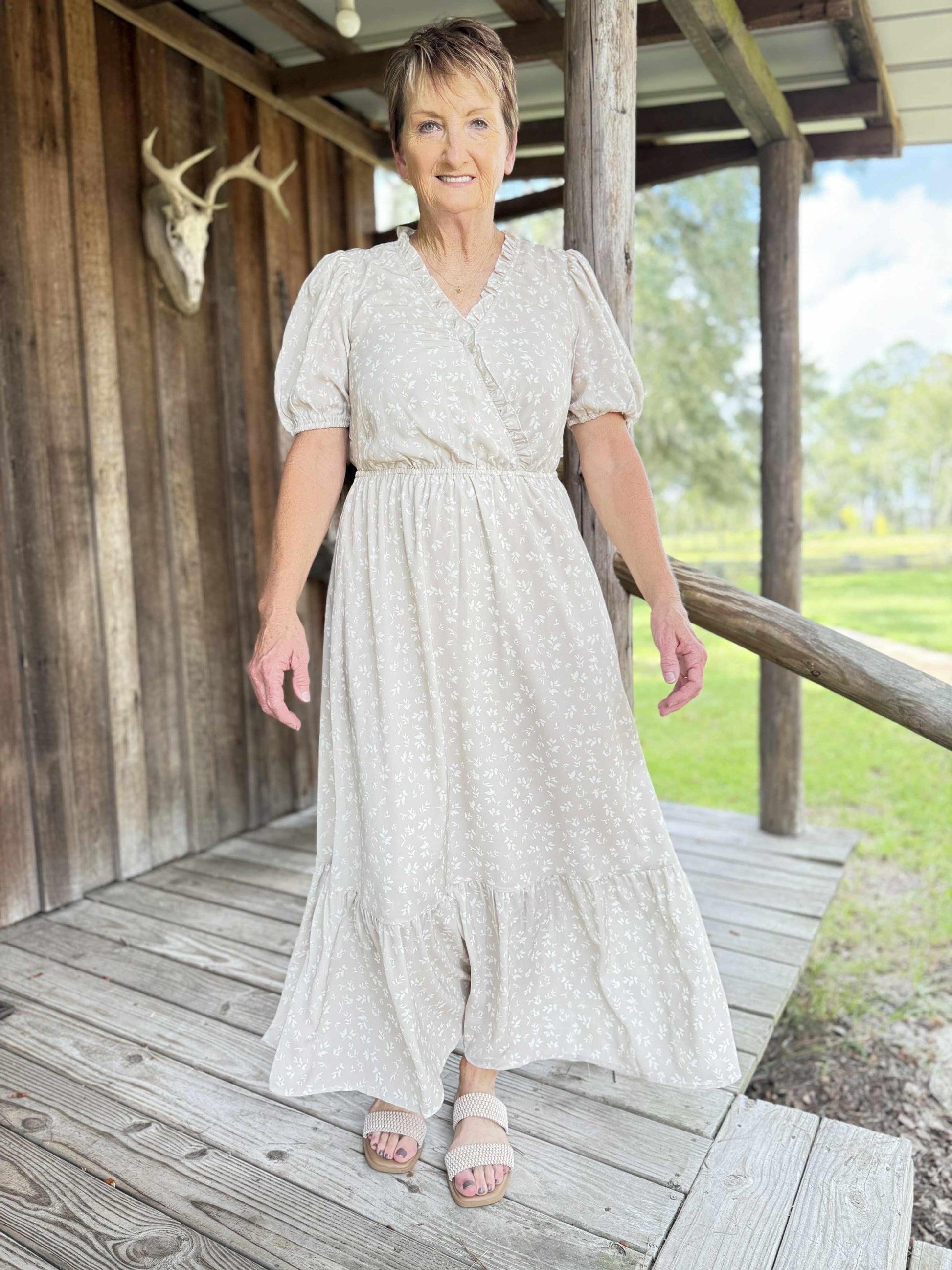 Woman wearing a cream floral wrap maxi dress with puff sleeves and tiered hem, styled outdoors.