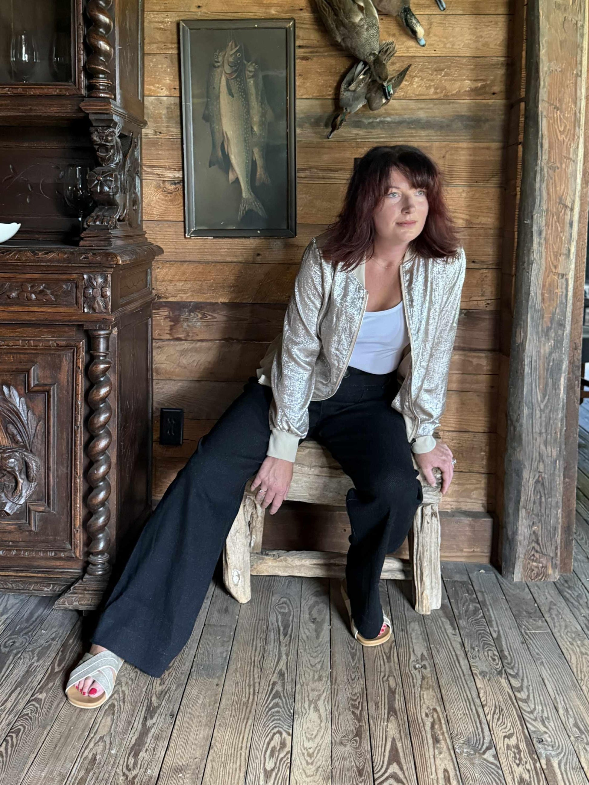 Woman wearing a metallic gold zip-up bomber-style jacket with ribbed cuffs and hem, styled with black wide-leg pants.