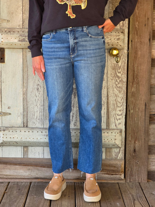 Person wearing blue jeans and brown shoes standing in front of a wooden door.