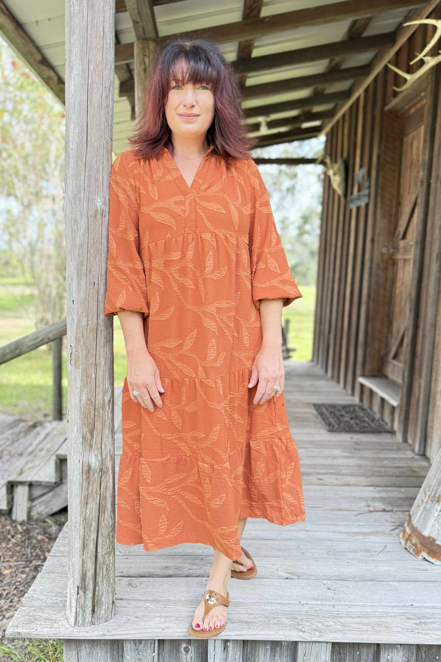 Woman in an orange dress standing on a wooden porch.