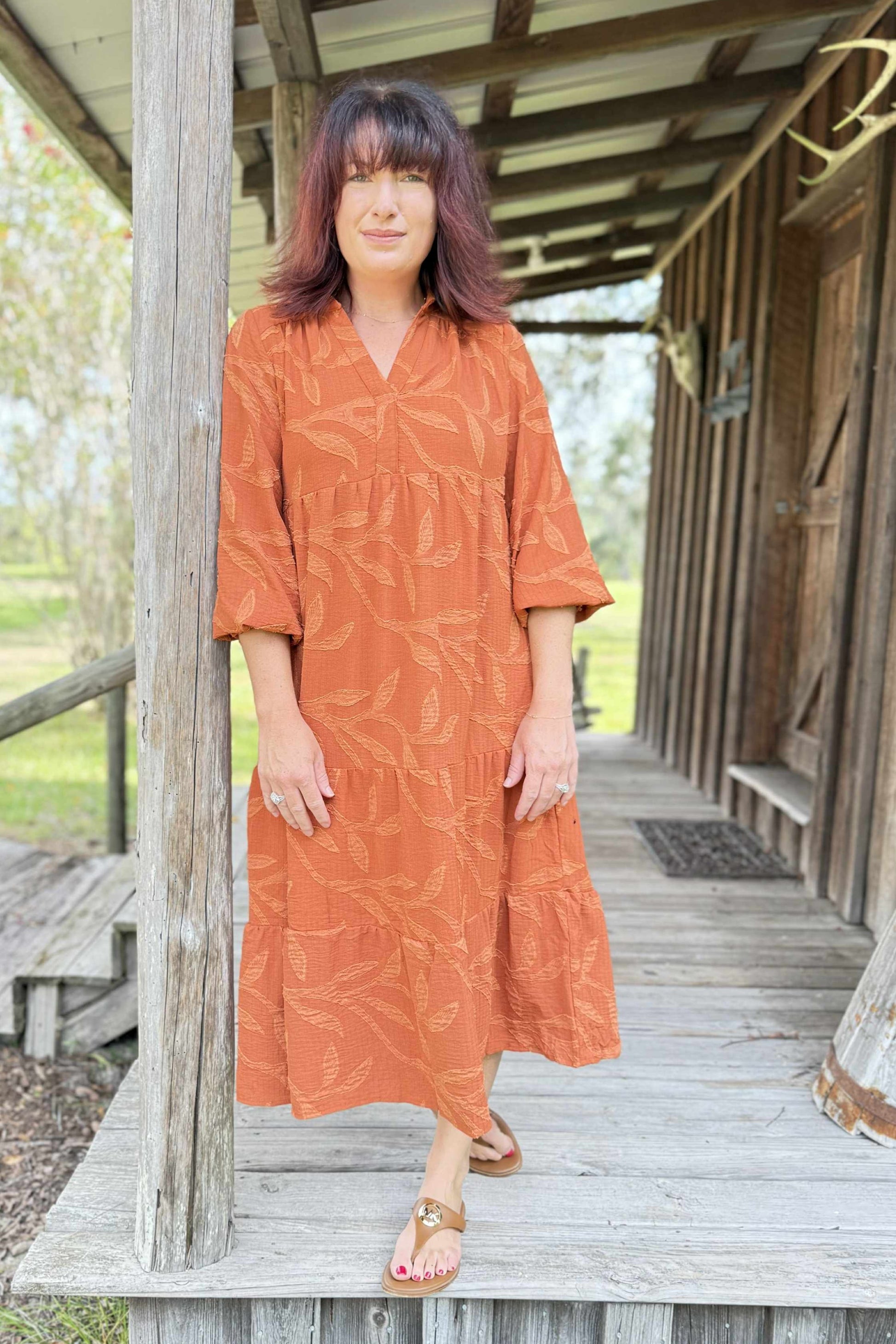 Woman in an orange dress standing on a wooden porch.