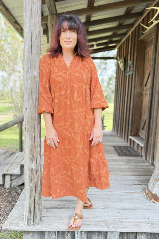 Woman in an orange dress standing on a wooden porch.