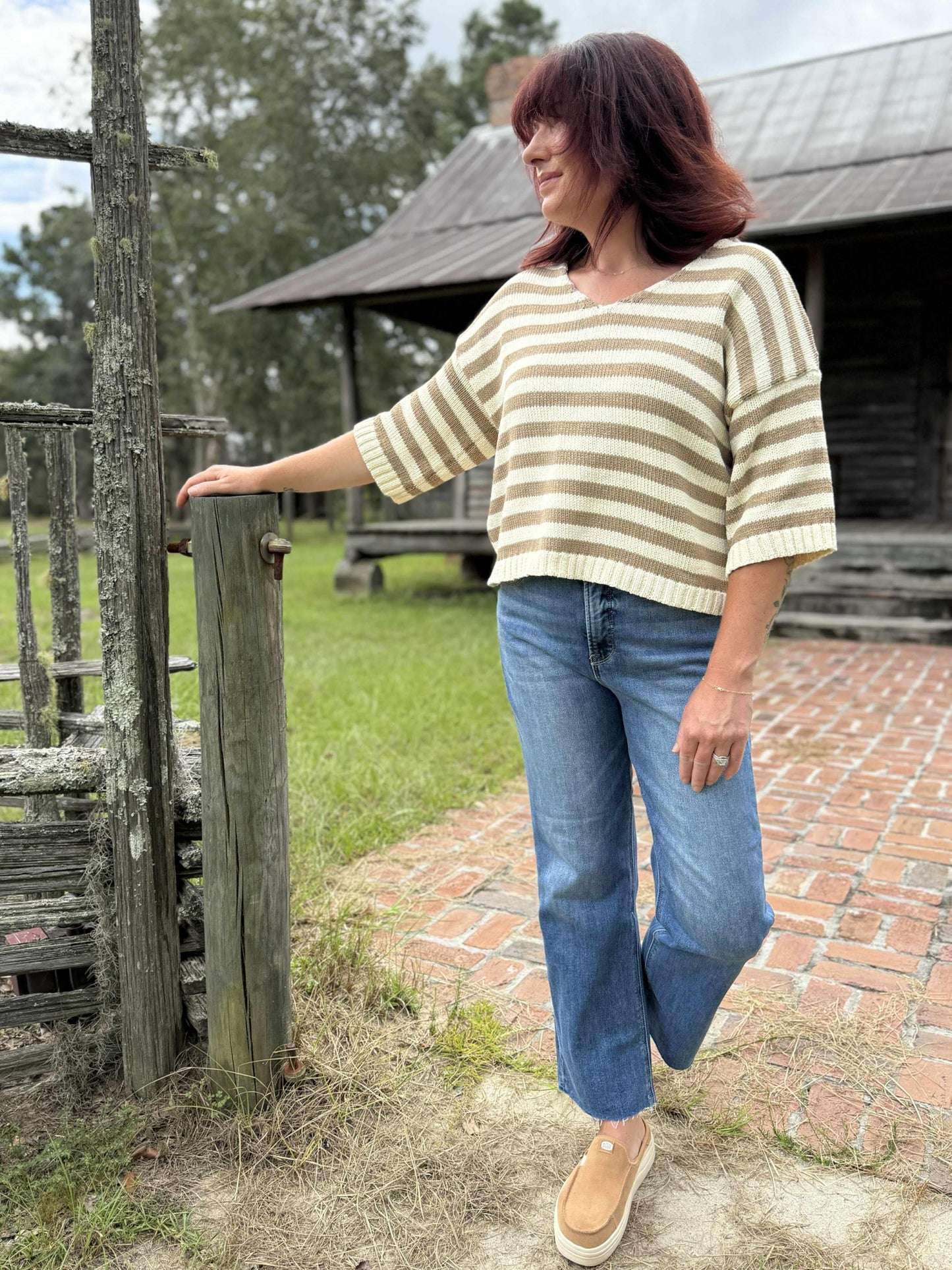 Woman wearing a beige and cream striped short-sleeve V-neck knit top with relaxed fit, paired with blue jeans outdoors.