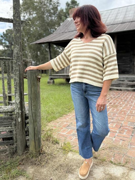 Woman wearing a beige and cream striped short-sleeve V-neck knit top with relaxed fit, paired with blue jeans outdoors.