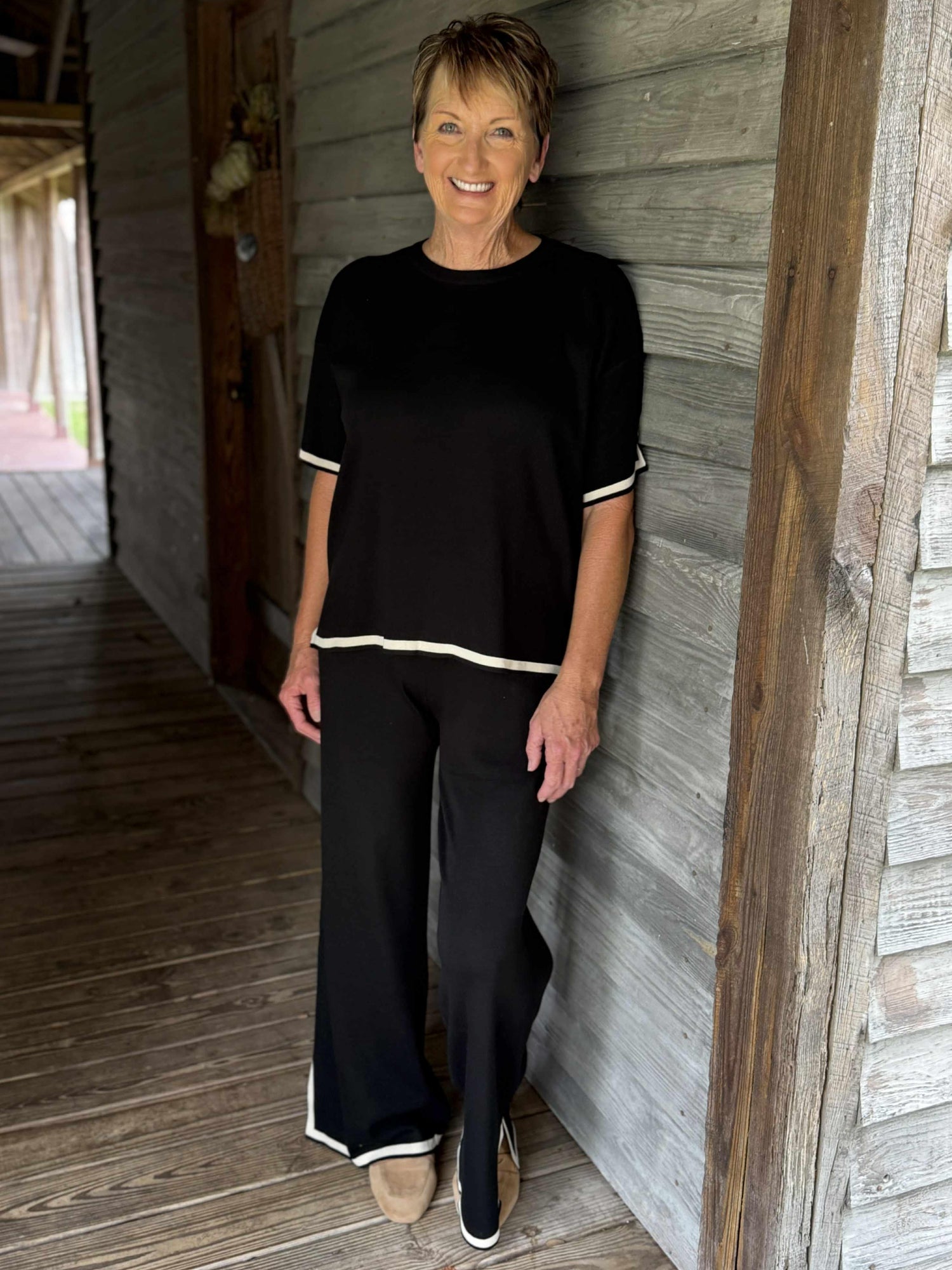 Woman wearing a black two-piece knit lounge set with wide-leg pants and short-sleeve top trimmed in ivory.